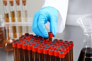 Photo of Scientist taking test tube with brown liquid from stand, closeup