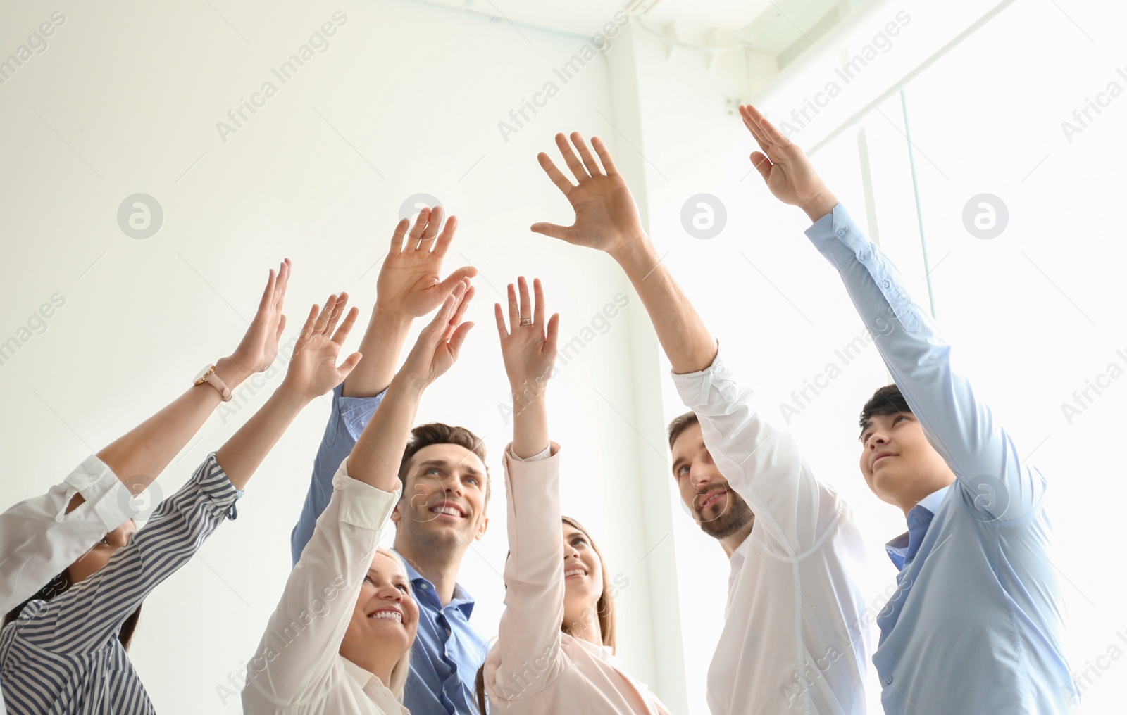 Photo of People raising hands together indoors. Unity concept