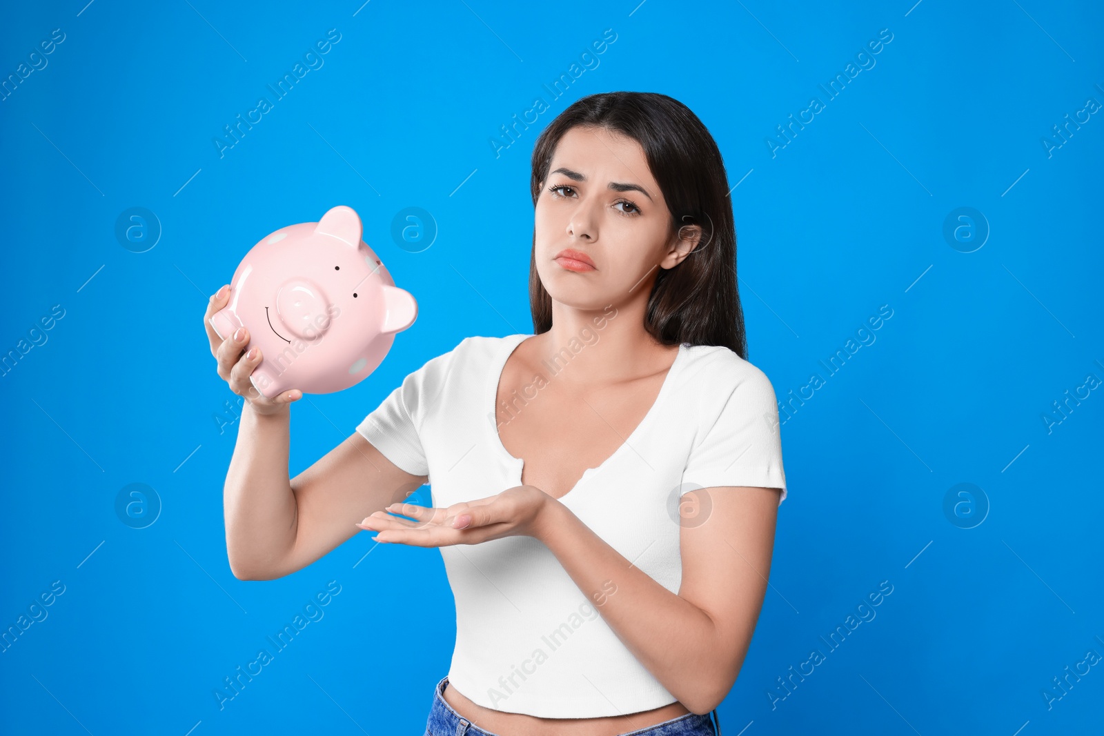 Photo of Sad young woman with piggy bank on light blue background