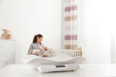 Photo of Modern baby scales on table and blurred woman with child indoors. Space for text