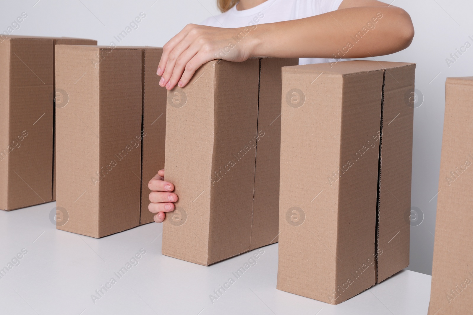 Photo of Woman folding cardboard boxes at white table, closeup. Production line