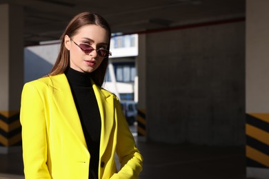 Photo of Fashionable young woman wearing stylish outfit with yellow jacket in open parking garage. Space for text