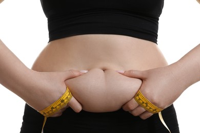 Photo of Woman with measuring tape touching belly fat on white background, closeup. Overweight problem