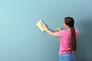 Photo of Young woman cleaning color wall with rag