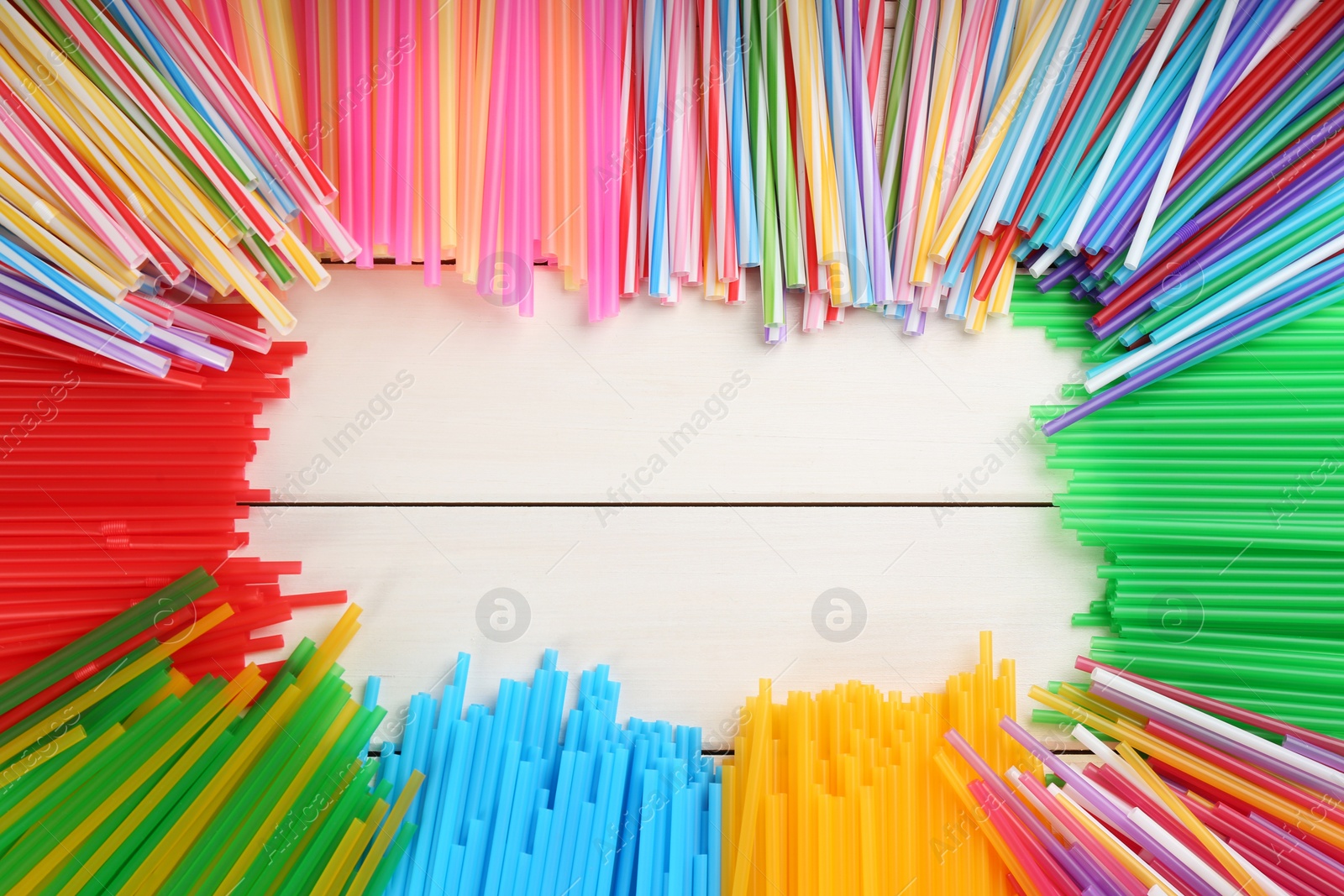 Photo of Frame of colorful plastic drinking straws on white wooden table, flat lay. Space for text