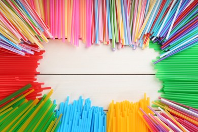 Photo of Frame of colorful plastic drinking straws on white wooden table, flat lay. Space for text