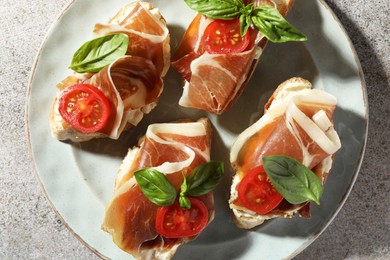 Tasty sandwiches with cured ham, basil and tomatoes on grey table, top view