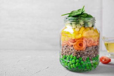 Photo of Healthy salad in glass jar on light table. Space for text