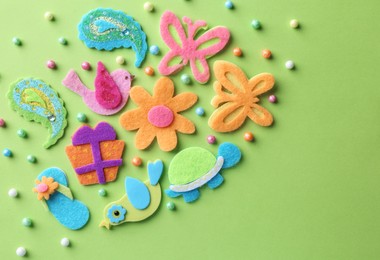 Photo of Different small colorful felt items and beads on green background, flat lay