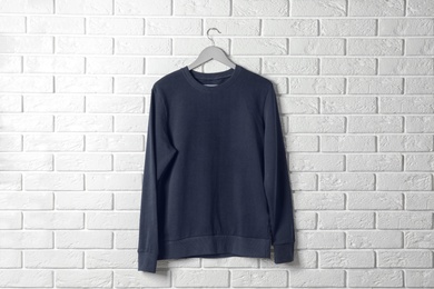 Photo of Hanger with dark sweatshirt against brick wall. Mockup for design