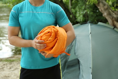 Image of Young man holding sleeping bag near camping tent outdoors, closeup