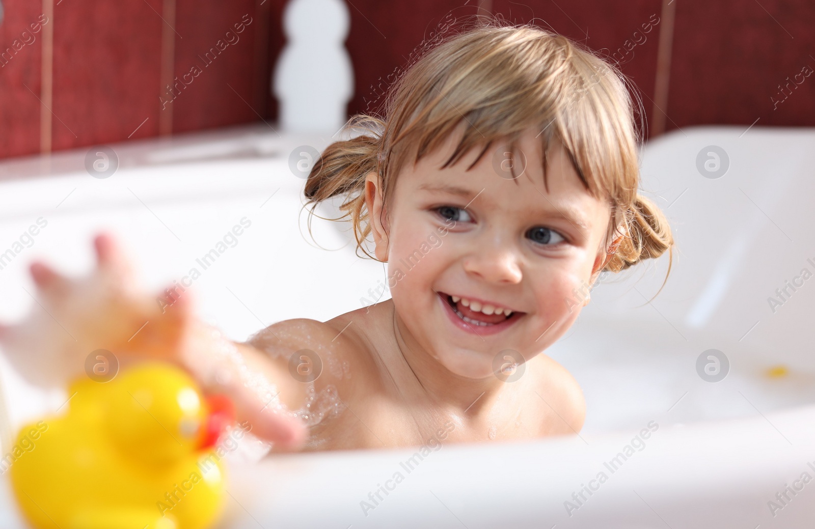 Photo of Smiling girl taking toy duck in bathtub at home, selective focus