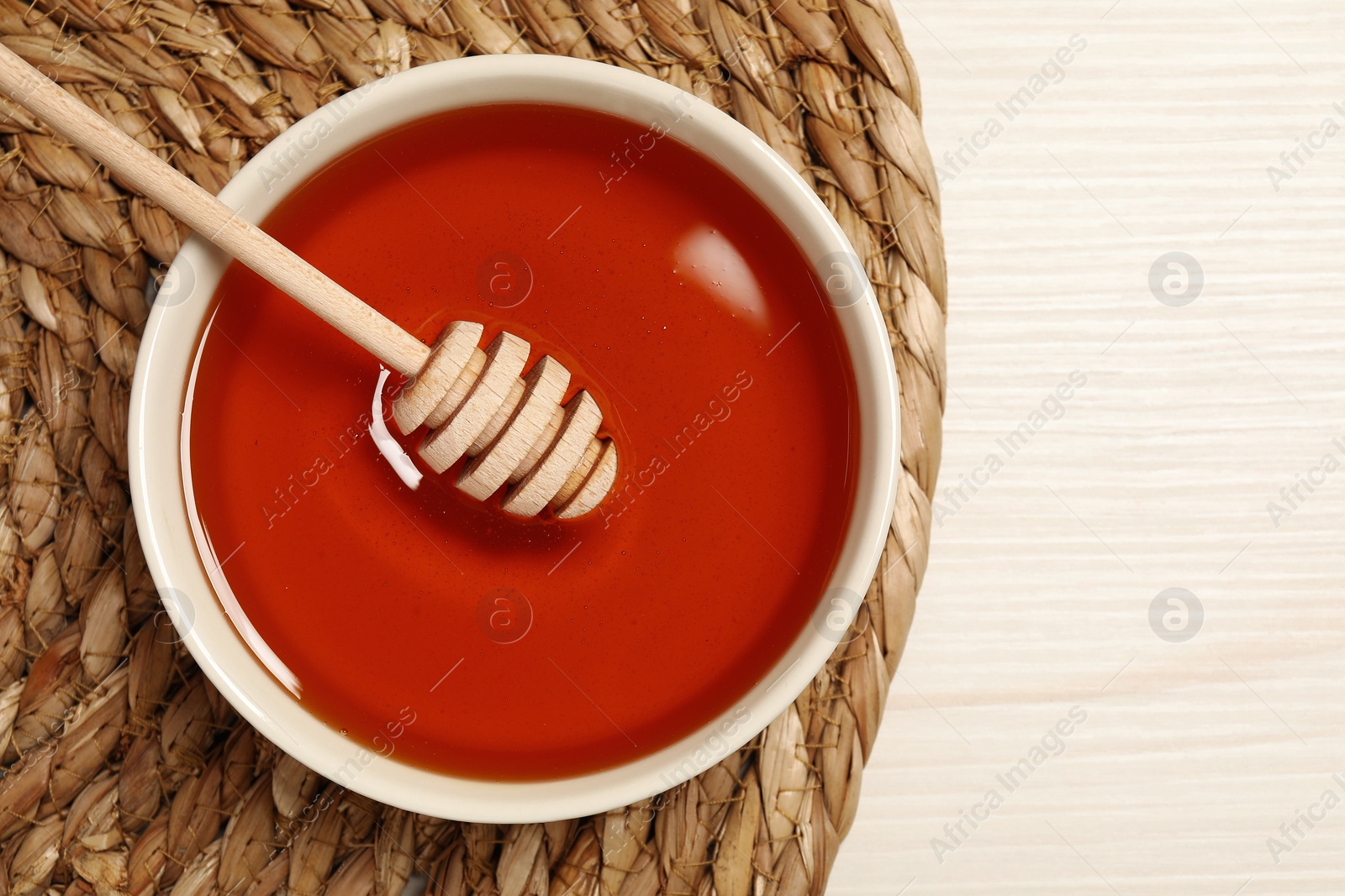 Photo of Bowl with tasty honey and dipper on white wooden table, top view. Space for text