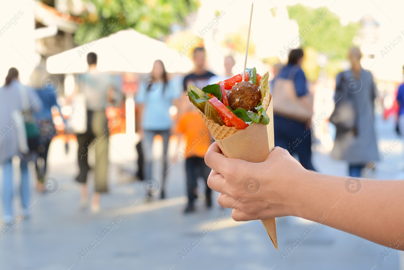 Photo of Woman holding wafer with falafel and vegetables outdoors, closeup. Space for text