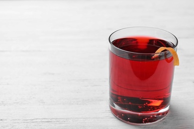 Glass of tasty refreshing cocktail with orange peel on while wooden table. Space for text