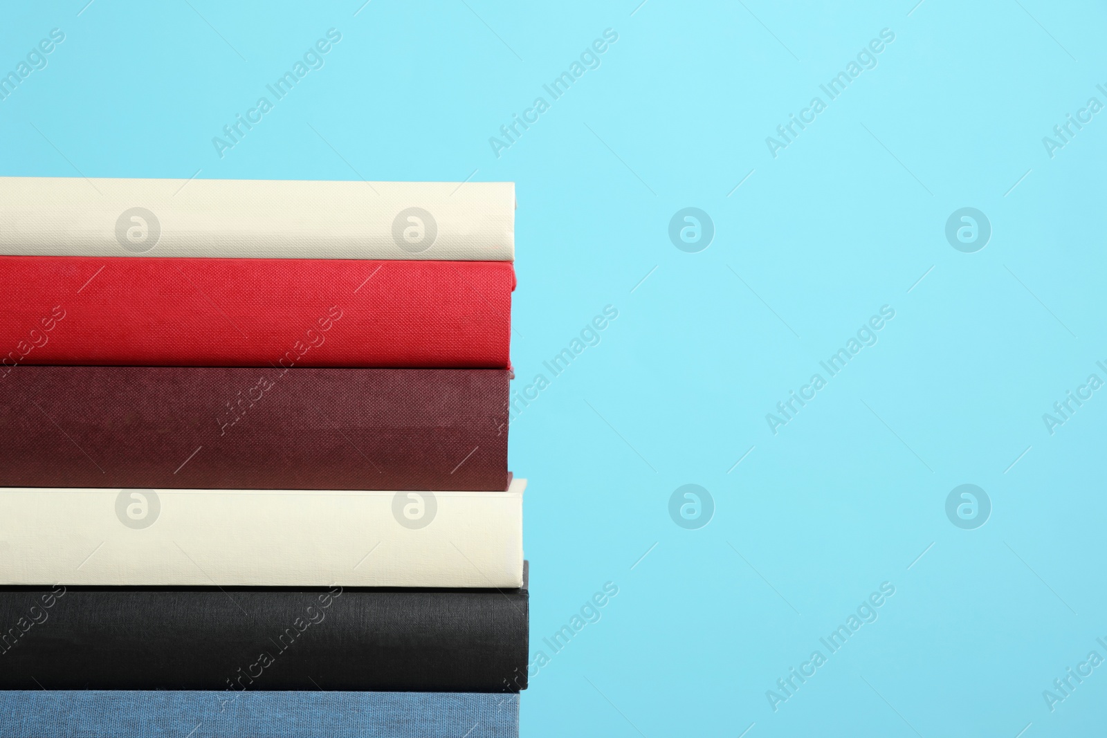 Photo of Stack of hardcover books on light blue background, space for text