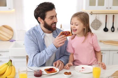 Photo of Father and his cute little daughter having breakfast at table in kitchen