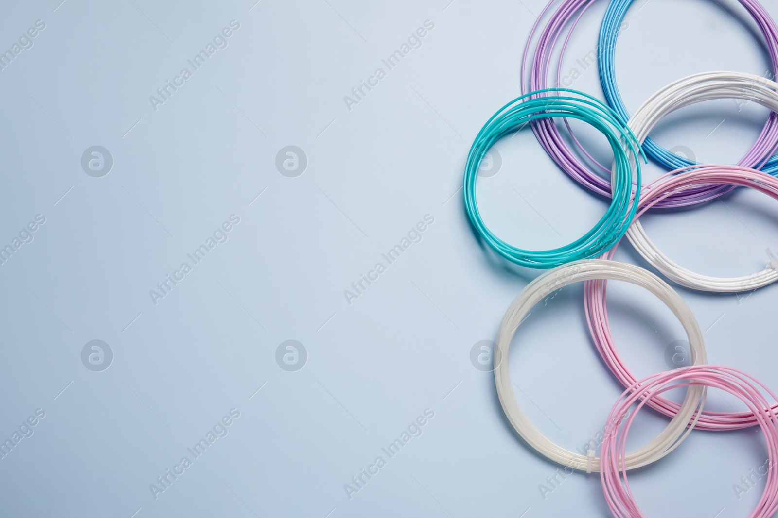 Photo of Colorful plastic filaments for 3D pen on light blue background, flat lay. Space for text