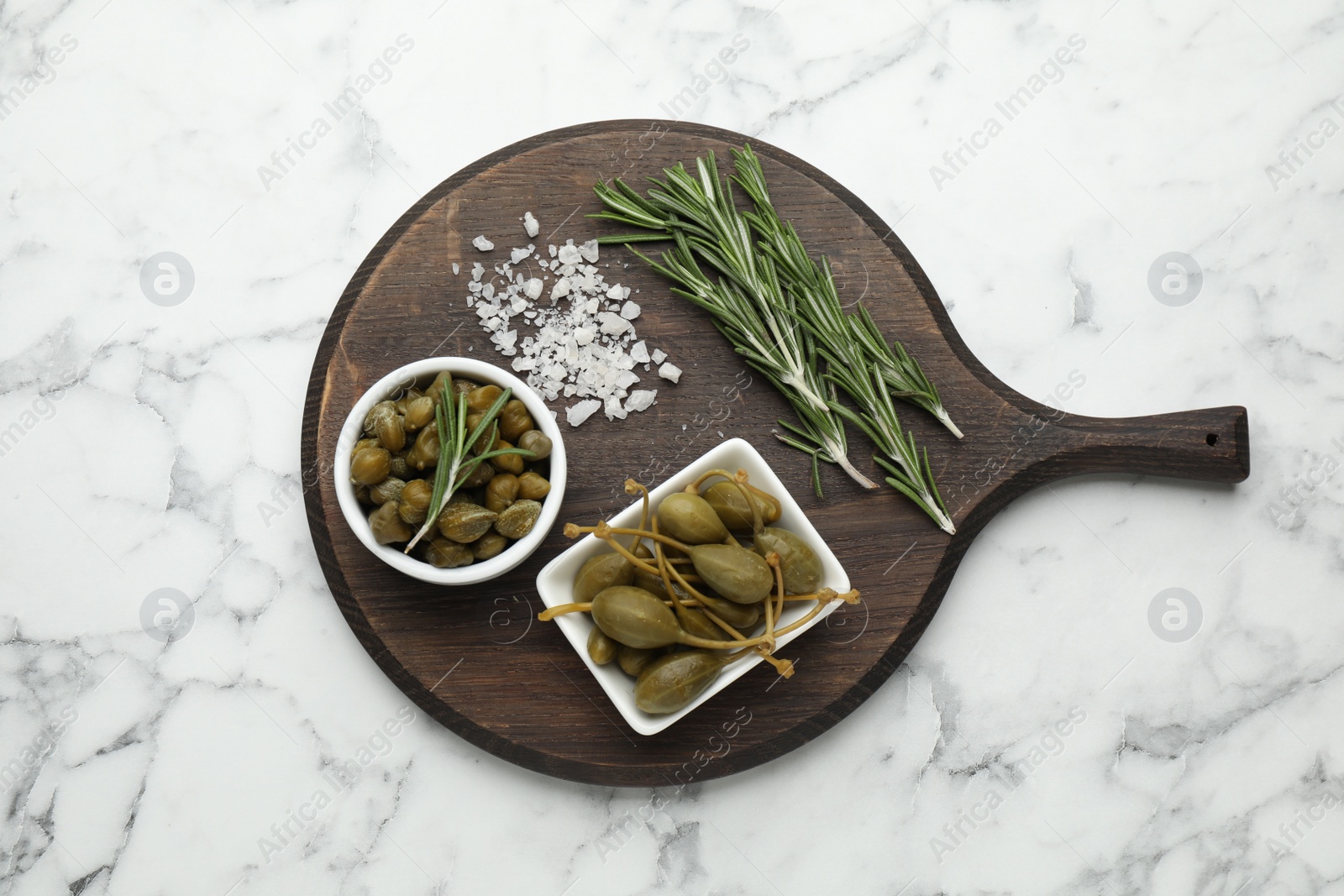 Photo of Delicious pickled capers, salt and rosemary twigs on white marble table, top view