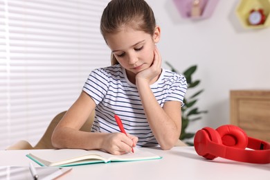 Photo of E-learning. Cute girl taking notes while studying online at table indoors