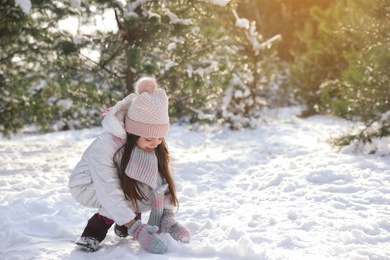 Photo of Cute little girl rolling snowball in winter forest