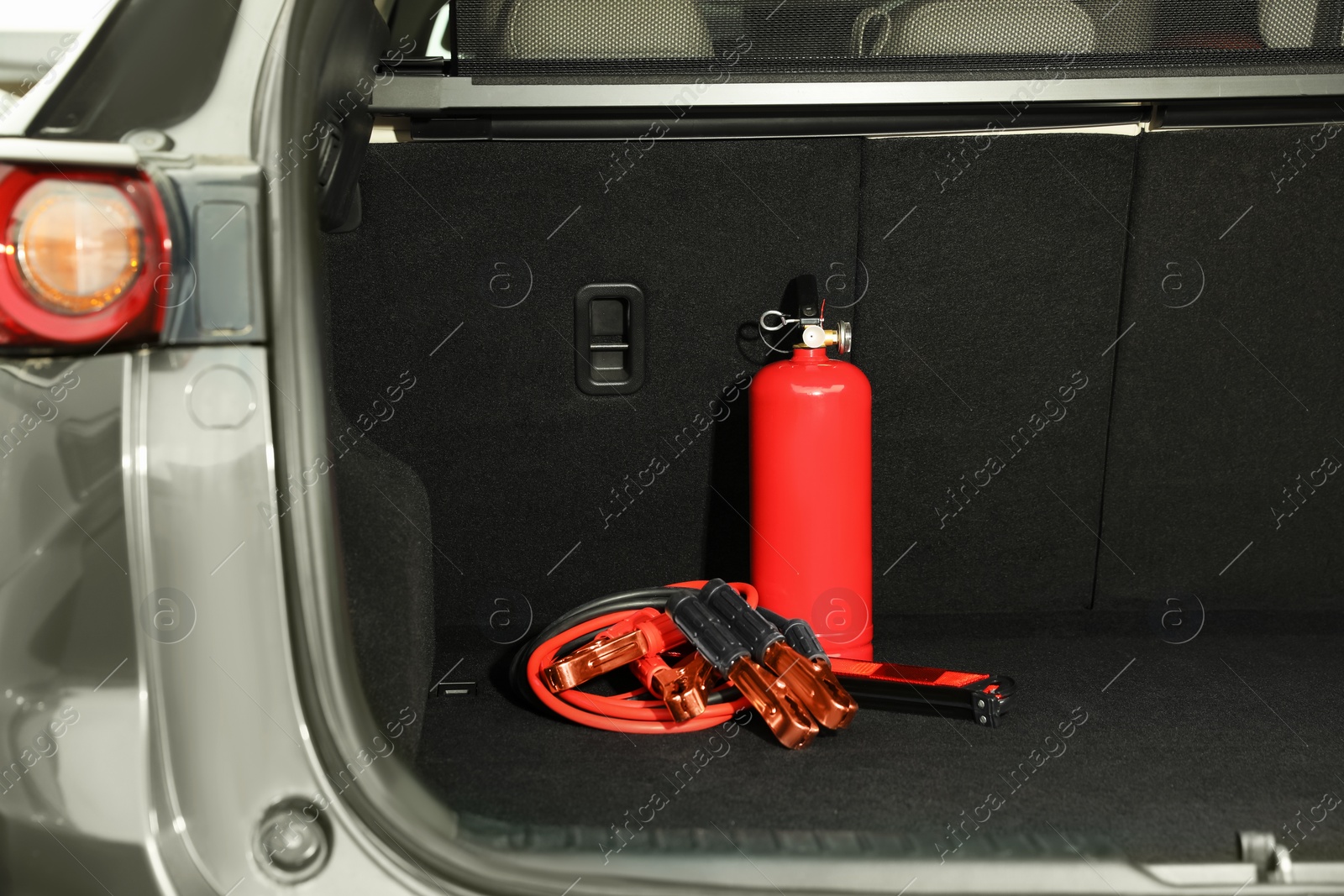 Photo of Red fire extinguisher and battery jumper cables in trunk. Car safety