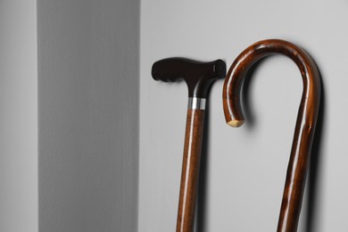 Different walking canes near light grey wall, closeup. Space for text