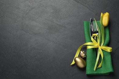 Photo of Cutlery set, painted eggs and beautiful flower on black table, flat lay with space for text. Easter celebration