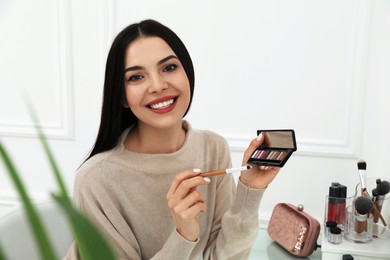 Photo of Beautiful happy woman applying makeup in room