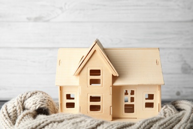 Photo of Plywood toy house with warm scarf on table against light background. Heating system