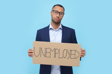 Photo of Young man holding sign with word Unemployed on light blue background