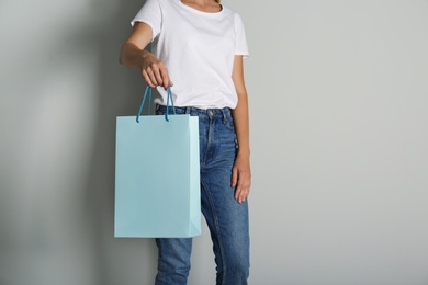 Photo of Woman with paper shopping bag on light grey background, closeup