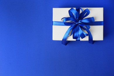 Beautiful gift box with bow on blue background, top view. Space for text
