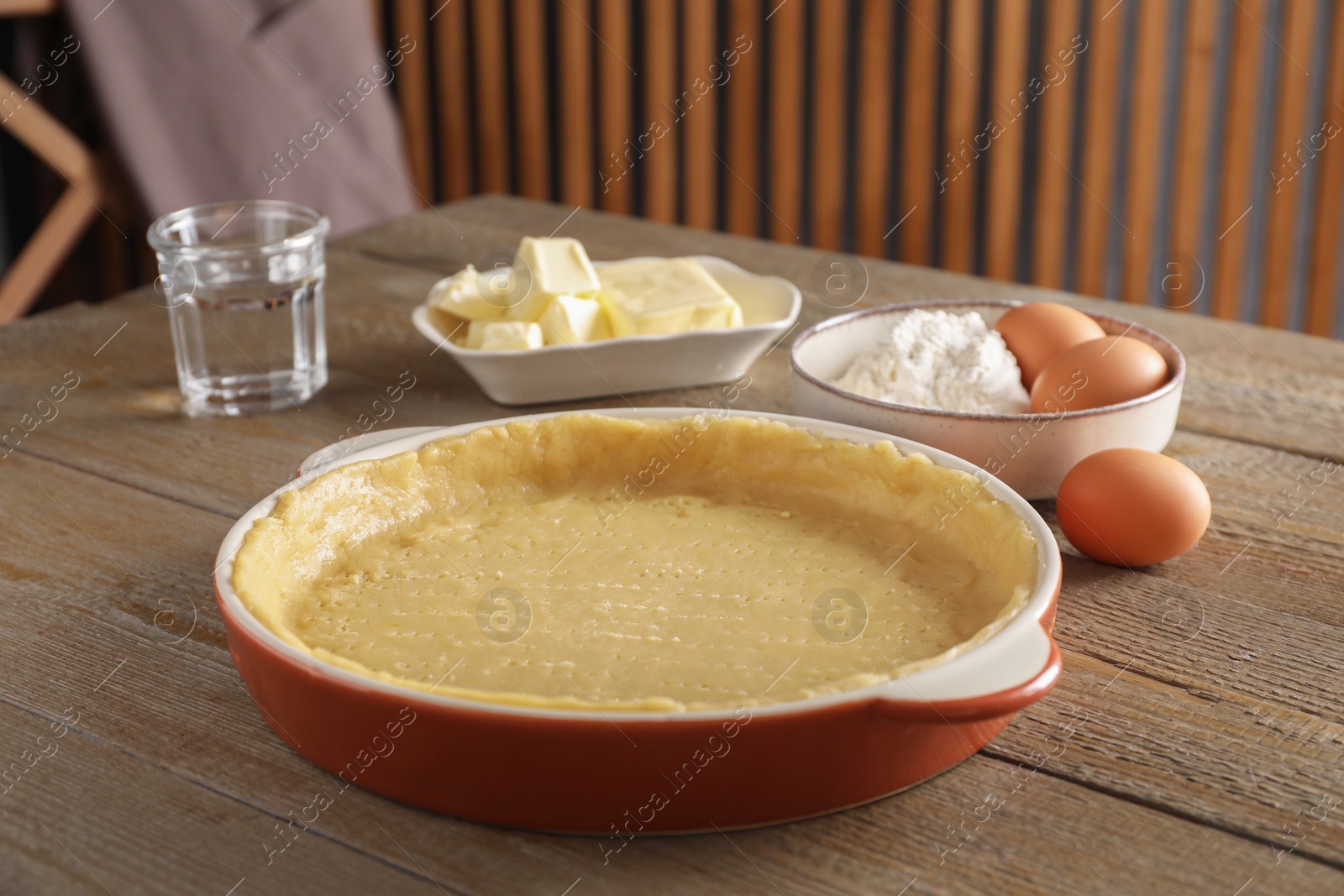 Photo of Making quiche. Baking dish with fresh dough and ingredients on wooden table