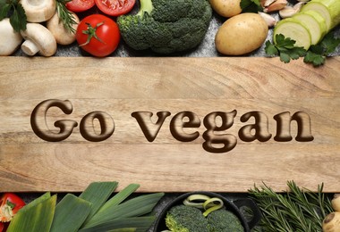 Image of Wooden board with phrase Go Vegan and fresh vegetables on table, flat lay