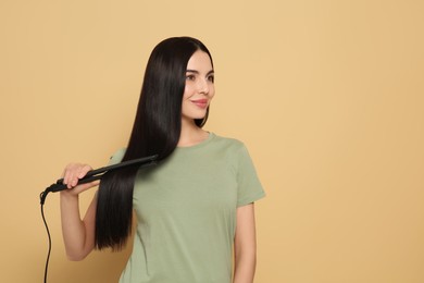 Photo of Beautiful happy woman using hair iron on beige background. Space for text