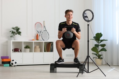 Photo of Smiling sports blogger training with kettlebell while streaming online fitness lesson at home