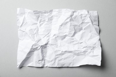 Sheet of white crumpled paper on grey background, top view