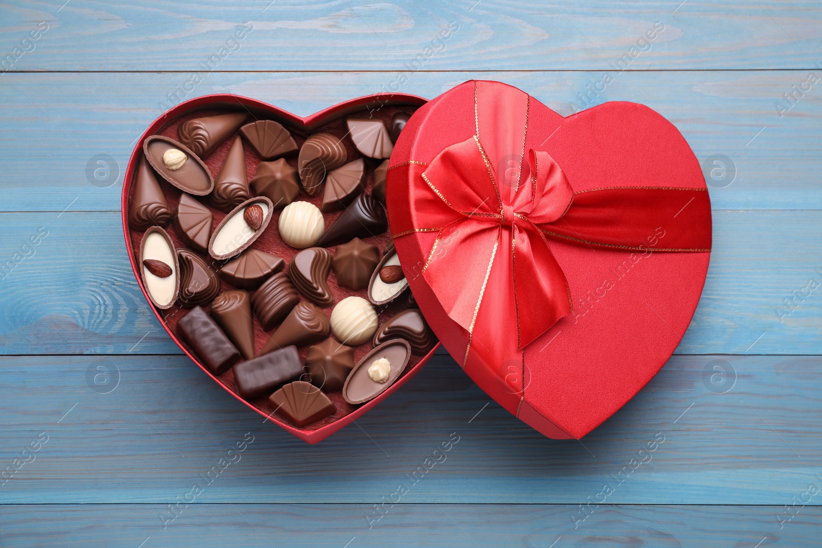 Photo of Heart shaped box with delicious chocolate candies on light blue wooden table, top view