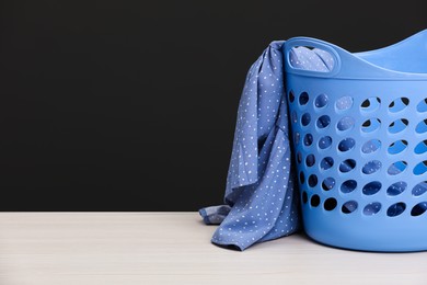 Photo of Plastic laundry basket with clothes near dark grey wall. Space for text