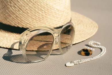 Photo of Stylish hat, sunglasses and jewelry on grey surface, closeup