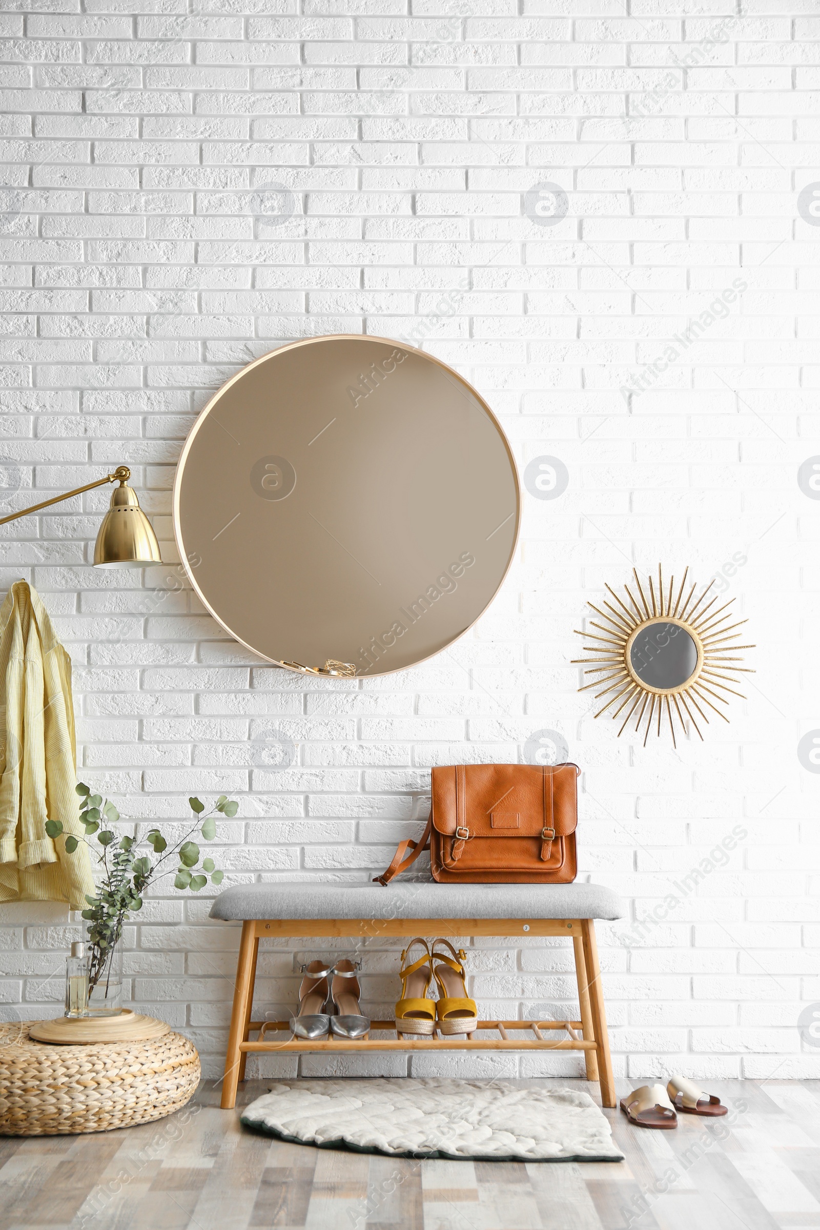 Photo of Hallway interior with big round mirror and shoe storage bench near brick wall