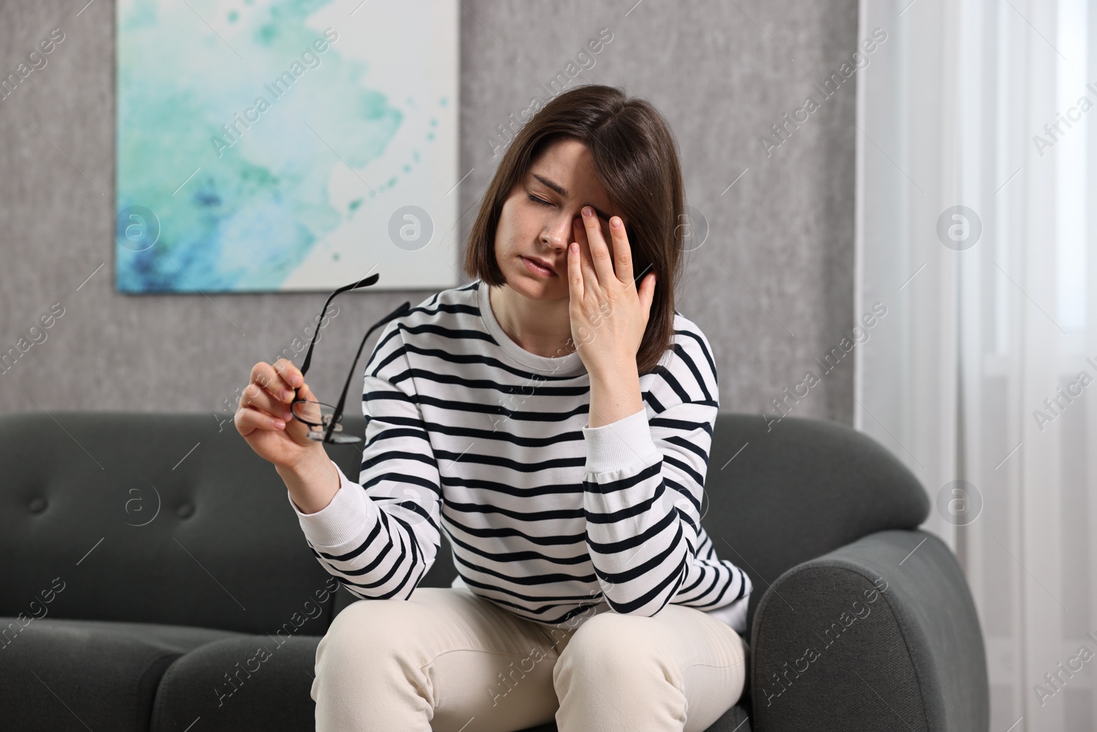 Photo of Overwhelmed woman with glasses sitting on sofa indoors