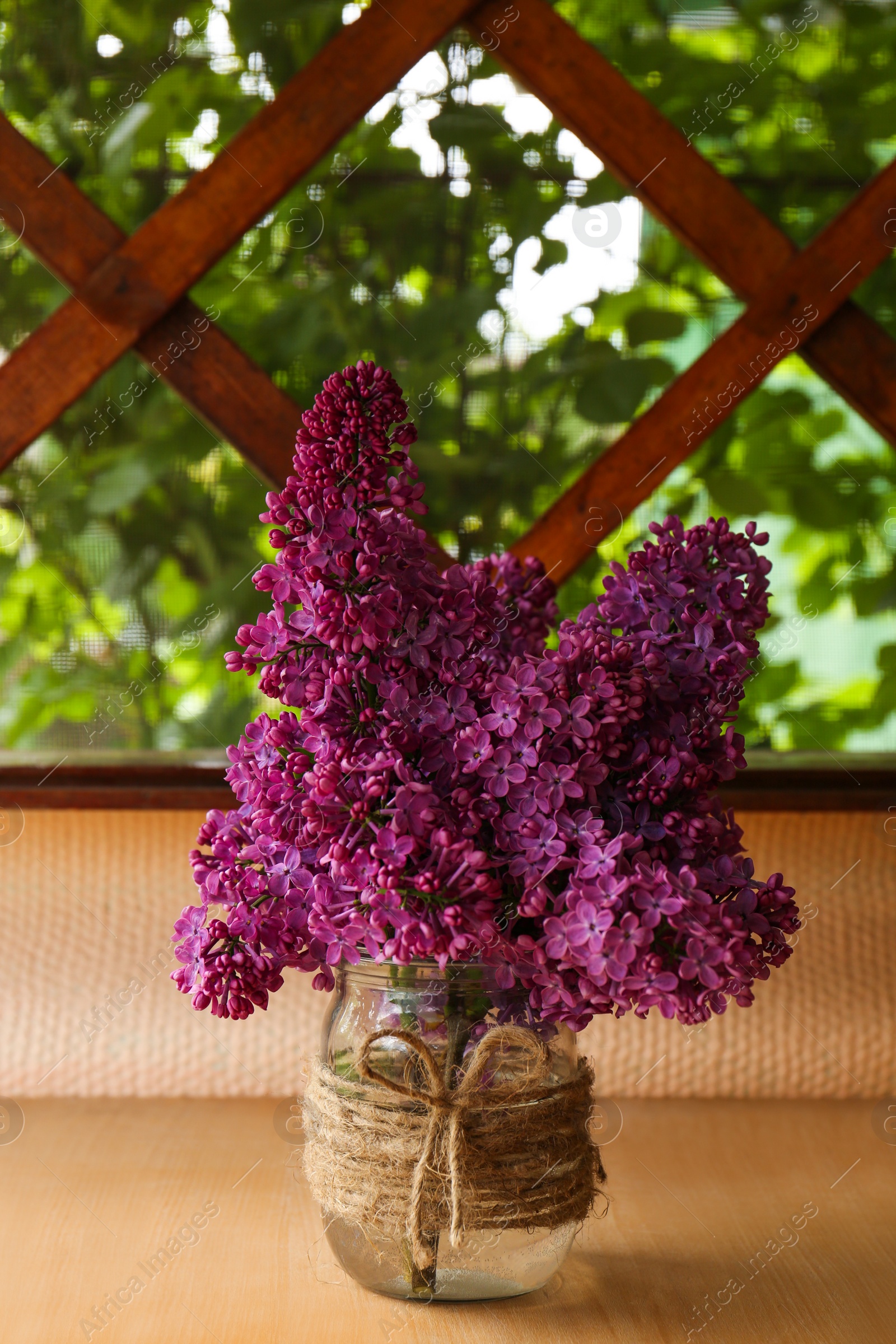 Photo of Beautiful lilac flowers in glass jar on wooden table indoors