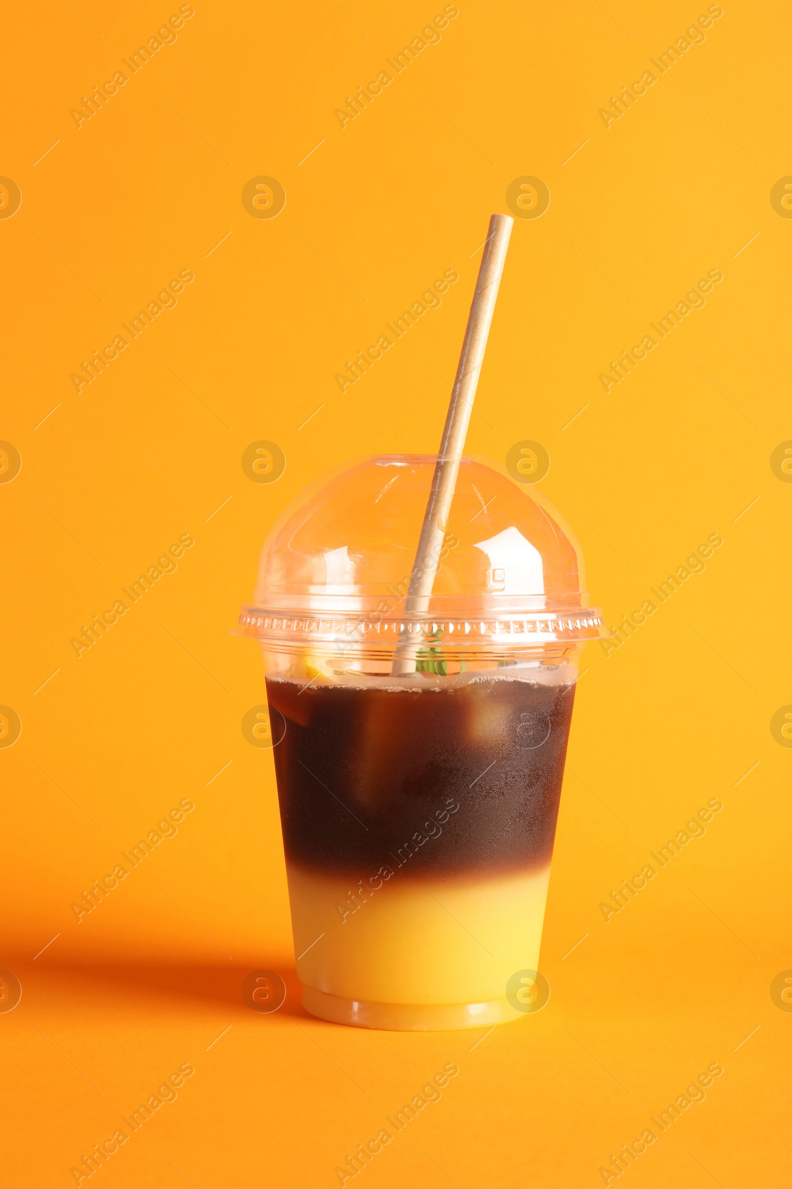 Photo of Tasty refreshing drink with coffee and orange juice in plastic cup on bright color background