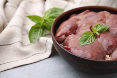 Photo of Bowl with raw chicken liver and basil on light grey table, closeup. Space for text