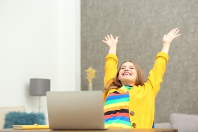 Happy young woman playing online lottery using laptop at home