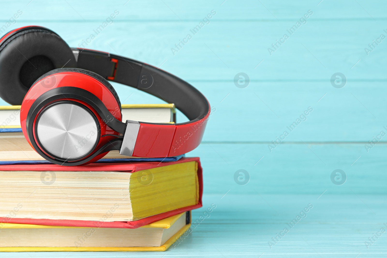 Photo of Books and modern headphones on light blue wooden table, closeup. Space for text