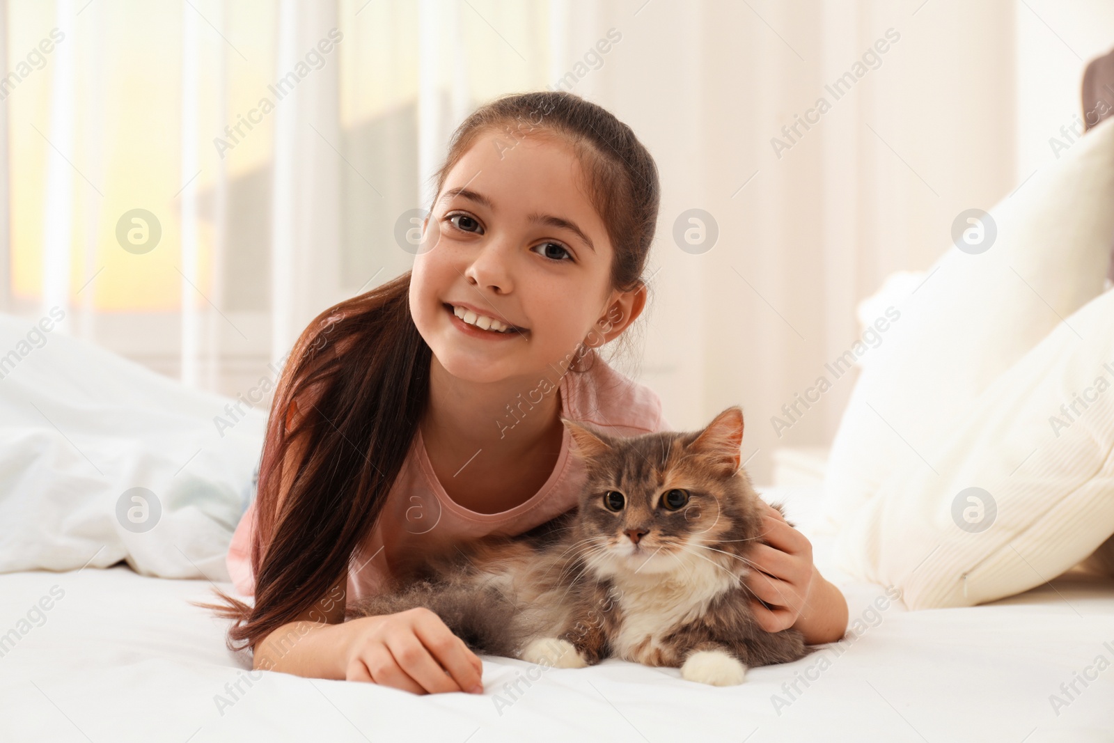 Photo of Cute little girl with cat lying on bed at home. First pet