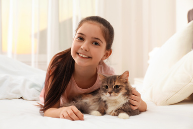 Photo of Cute little girl with cat lying on bed at home. First pet